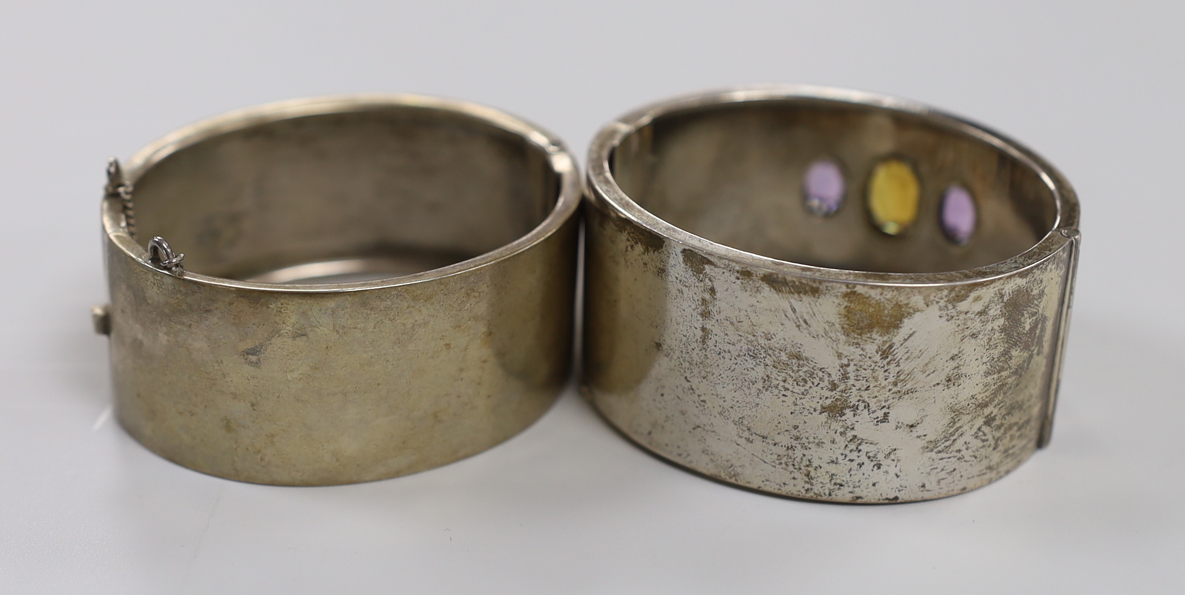 A late Victorian silver and three stone amethyst and citrine set hinged bangle and a later white metal bangle.